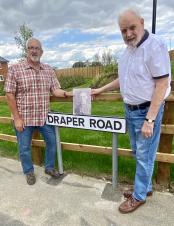 Gary Salmon and Geoff Moore standing at a new road sign for Draper Road, holding a picture of WW1 soldier William Ernest Draper, for whom the road is named